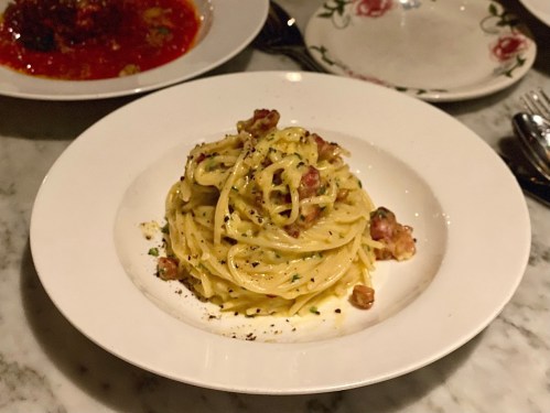 A plate of creamy spaghetti carbonara topped with crispy bacon bits, served on a white dish.