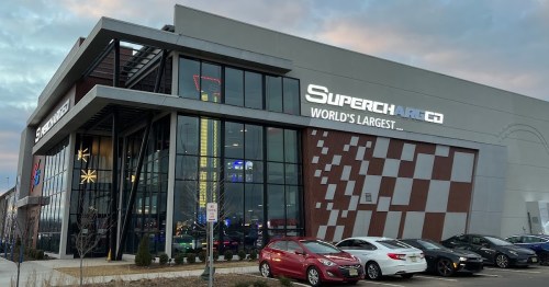 Exterior view of a modern building with "Supercharged" signage, featuring a large parking area and a cloudy sky.