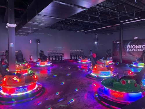 A dimly lit bumper car arena with colorful, illuminated cars and a few people enjoying the ride.