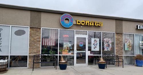 Exterior of a donut shop with a colorful sign, "AMARO'S DONUTS," featuring an open sign and American flag in the window.