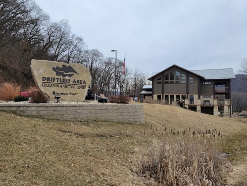 Sign for Driftless Area Education & Visitors Center with a modern building and natural landscape in the background.