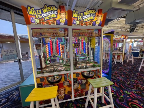 Two colorful arcade machines themed after "Willy Wonka & the Chocolate Factory," with bright lights and stools.