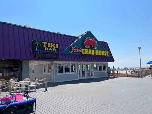 Exterior of Jake's Crab House and Tiki Bar on a sunny day, with beachgoers in the background.