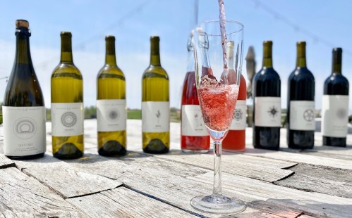 A glass filled with sparkling wine in front of various bottles of wine on a rustic wooden table.