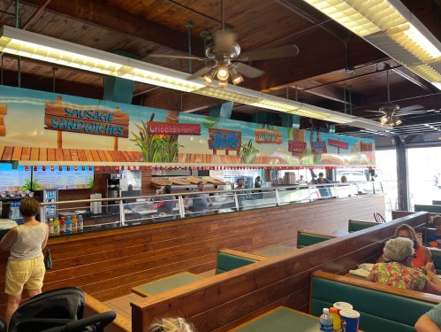 Interior of a casual eatery with a long counter, menu signs, and customers seated at green booths.