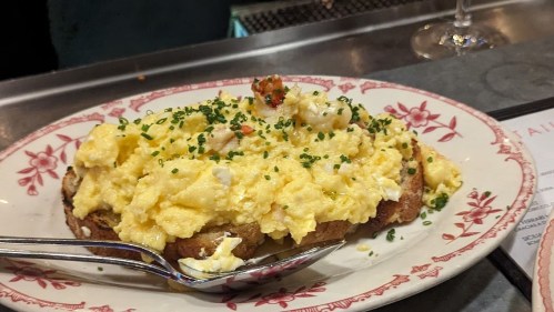 A plate of scrambled eggs with herbs and shrimp served on toasted bread, garnished with chives.