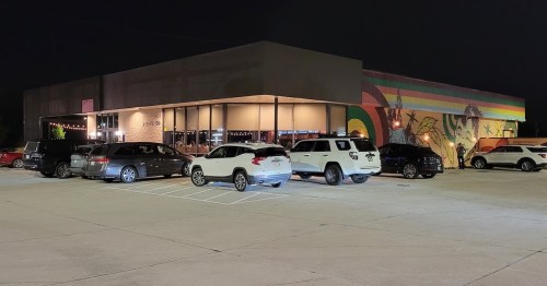 A dimly lit restaurant at night with parked cars and a colorful mural on the side.