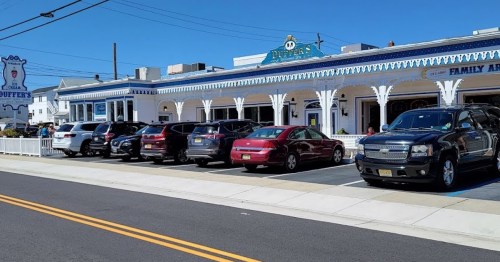 A row of parked cars in front of a large, blue and white restaurant on a sunny day.