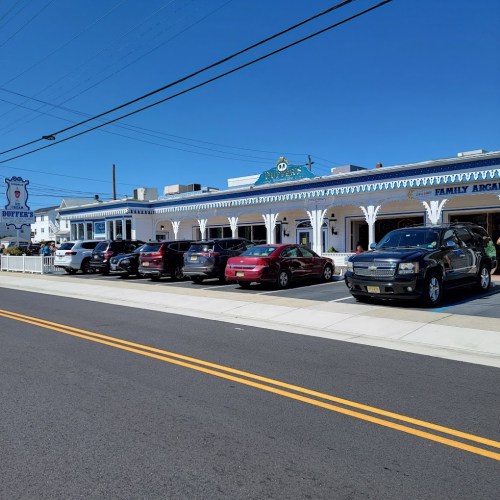 A row of parked cars in front of a white building with blue trim, under a clear blue sky.