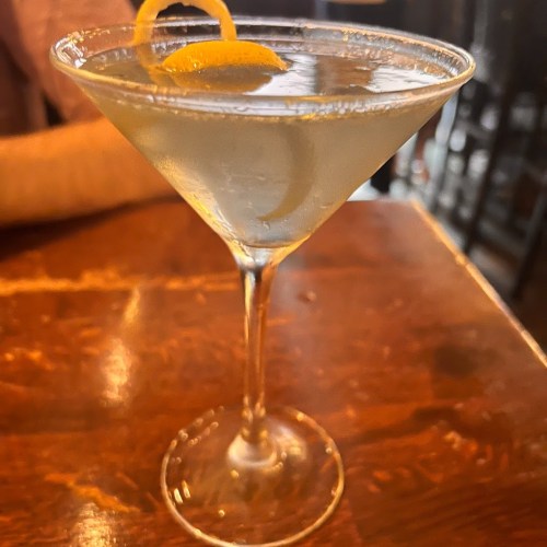 A close-up of a martini glass with a lemon twist, sitting on a wooden table.