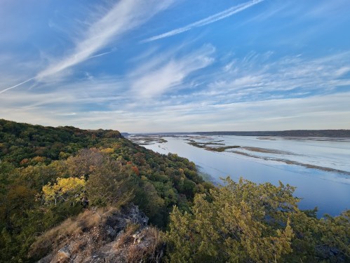 A scenic view of a river winding through lush green hills under a blue sky with wispy clouds.