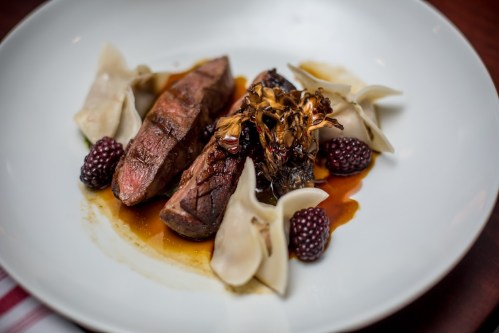 A plate featuring sliced steak, mushrooms, dumplings, and blackberries in a rich sauce.