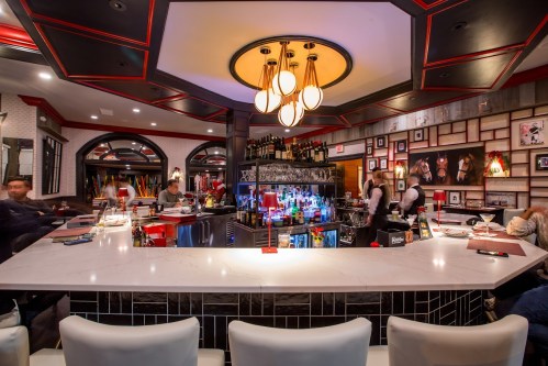 A stylish bar with a marble countertop, colorful liquor display, and modern lighting in a vibrant restaurant setting.