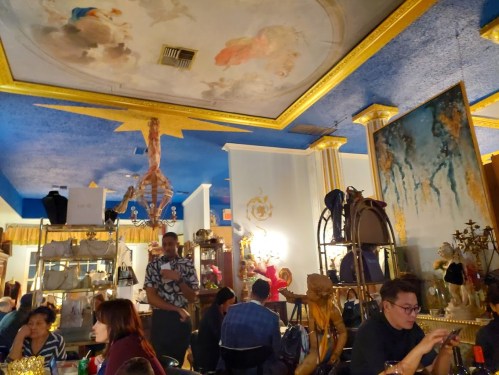 A vibrant restaurant interior with colorful decor, featuring a painted ceiling and patrons dining at tables.
