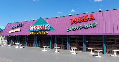 Colorful restaurant facade featuring signs for a lobster house, sushi bar, and pizza. Outdoor seating visible.