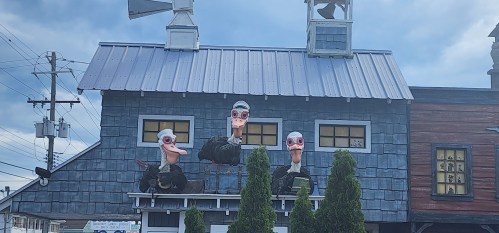 Three large, whimsical duck figures with exaggerated features on a building, surrounded by greenery and a cloudy sky.