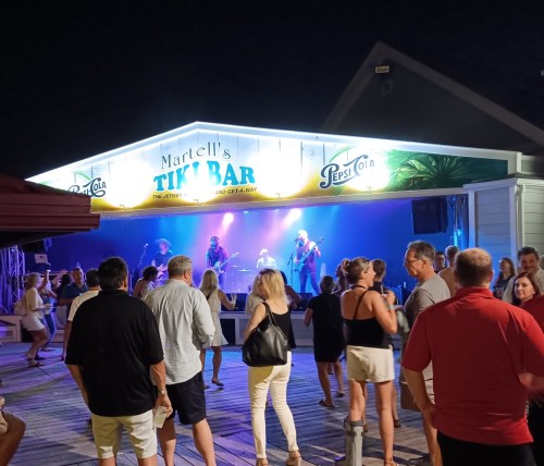 A lively outdoor bar scene at night with a band performing, surrounded by a crowd enjoying the music.