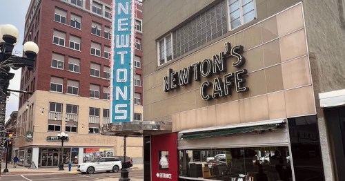Exterior view of Newton's Cafe, featuring a retro sign and nearby buildings in an urban setting.