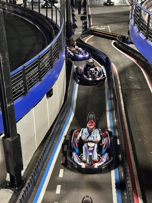 Go-karts racing on a winding track with blue barriers and a nighttime setting.
