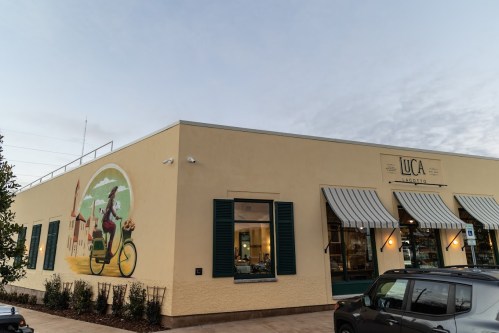 Exterior of a building with a mural of a woman on a bicycle, featuring green shutters and striped awnings.