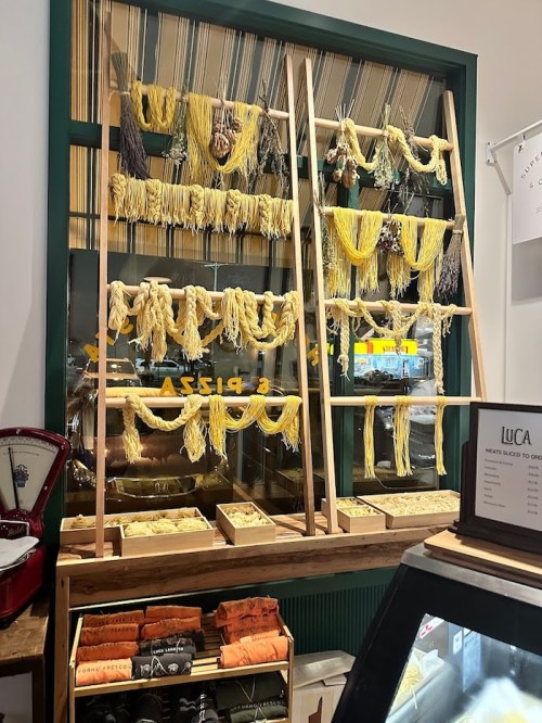 A display of hanging pasta in various shapes and colors, with a wooden rack and a glass case below.