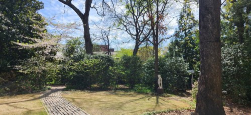 A serene garden scene with a stone path, lush greenery, and a statue under a clear blue sky.