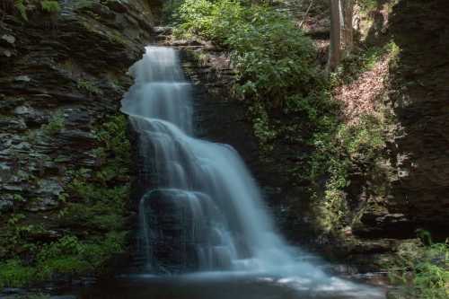 A serene waterfall cascades over rocky cliffs, surrounded by lush greenery and soft sunlight filtering through the trees.