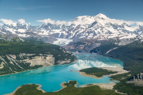 A stunning landscape featuring a turquoise lake surrounded by snow-capped mountains and lush green valleys.