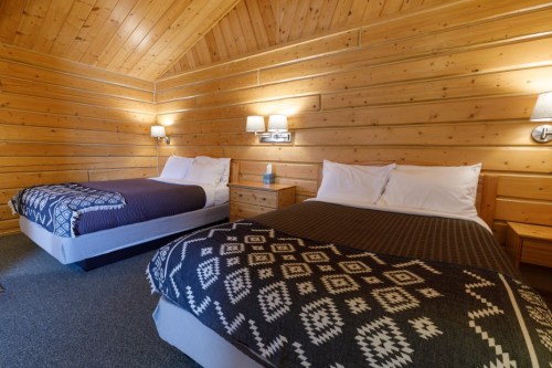 Cozy cabin interior featuring two beds with patterned blankets and wooden walls, creating a warm atmosphere.