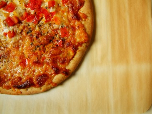 A freshly baked pizza with melted cheese and diced red peppers on a wooden surface.