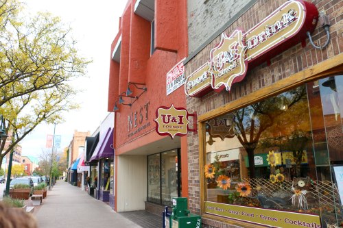 A street view featuring the U&I Lounge sign and nearby shops, with trees lining the sidewalk.
