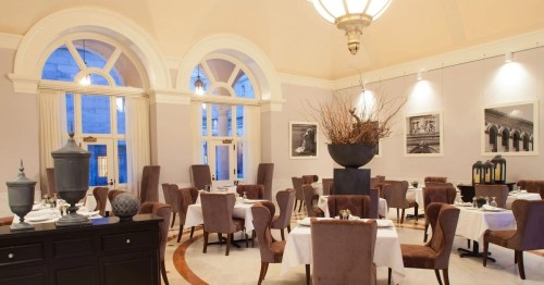 Elegant restaurant interior with tables set for dining, large windows, and decorative elements. Soft lighting enhances ambiance.