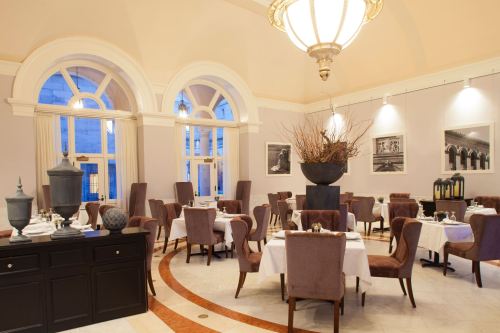 Elegant restaurant interior with arched windows, plush chairs, and tasteful decor, featuring tables set for dining.