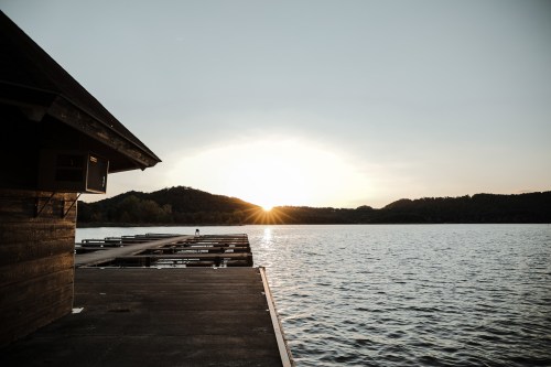 A serene lake at sunset, with a wooden dock extending into the water and hills in the background.