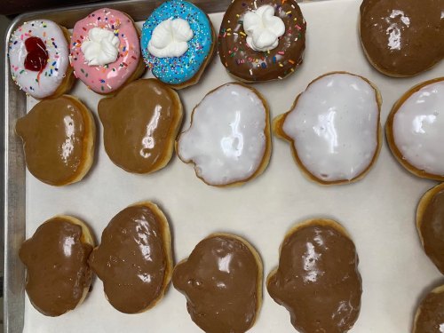 A tray of assorted donuts, including frosted, sprinkled, and glazed varieties, arranged on parchment paper.