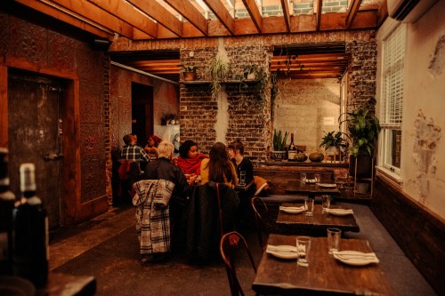 Cozy restaurant interior with wooden tables, plants, and patrons enjoying a meal in a warm, inviting atmosphere.
