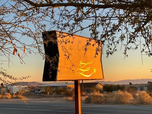 A weathered sign partially obscured by branches, with a sunset backdrop and desert landscape in the distance.