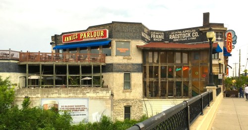 Historic buildings featuring shops and a restaurant, with outdoor seating and a bridge in the foreground.