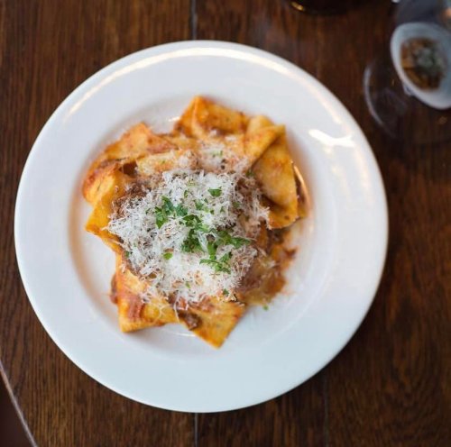 A plate of pasta topped with grated cheese and herbs, served on a wooden table.