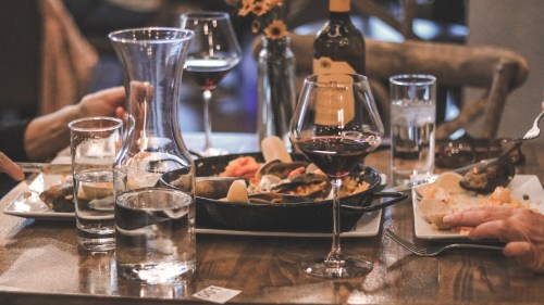 A table set with wine glasses, water, and a variety of dishes, including seafood and appetizers, in a cozy dining setting.