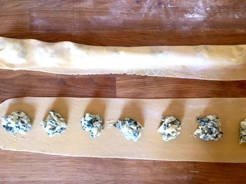 Fresh pasta dough with dollops of filling arranged along one edge, ready for shaping into ravioli.