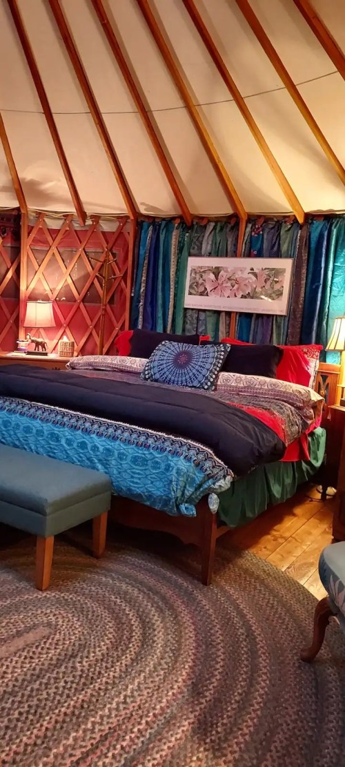 Cozy bedroom in a yurt with a colorful bedspread, decorative pillows, and warm lighting.