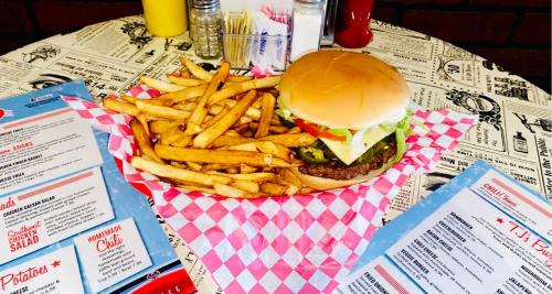 A burger with lettuce, tomato, and pickles served with a side of golden fries on a checkered paper plate.