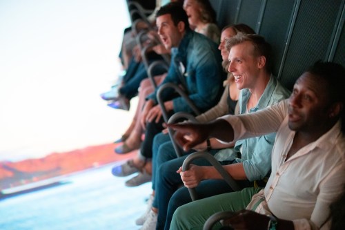 A group of people enjoying a thrilling ride, laughing and holding onto safety bars, with a scenic backdrop.
