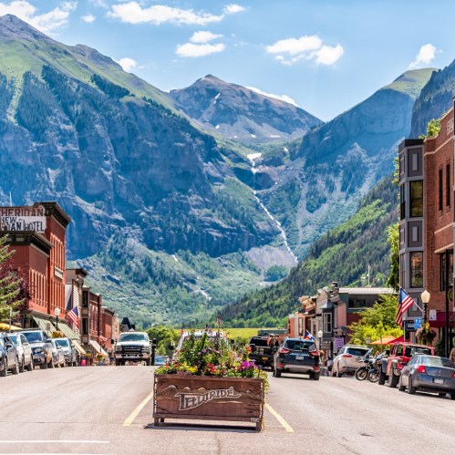 A scenic view of Telluride, Colorado, featuring mountains, a vibrant street, and flower planters in the foreground.