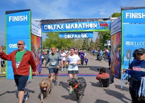 Participants crossing the finish line at the Colfax Marathon and 5K, with dogs and spectators in the background.