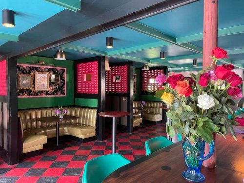 A vibrant café interior with green and red walls, cozy booths, and a colorful flower arrangement on a table.