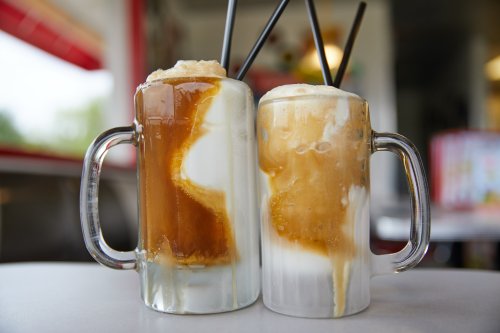 Two frosty mugs filled with root beer floats, featuring layers of root beer and creamy ice cream, topped with straws.