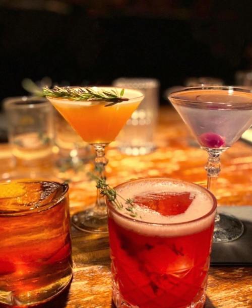A selection of colorful cocktails on a wooden table, featuring garnishes and elegant glassware.