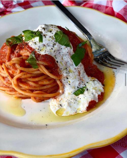 A plate of spaghetti topped with marinara sauce, dollops of ricotta, fresh basil, and a drizzle of olive oil.